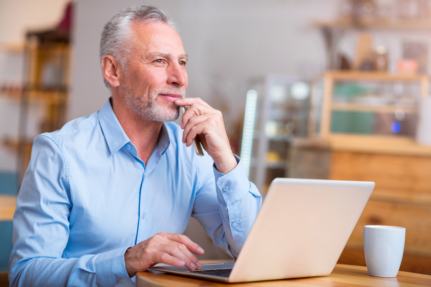 Mull it over. Thoughtful content senior man thinking and using laptop while sitting at the table